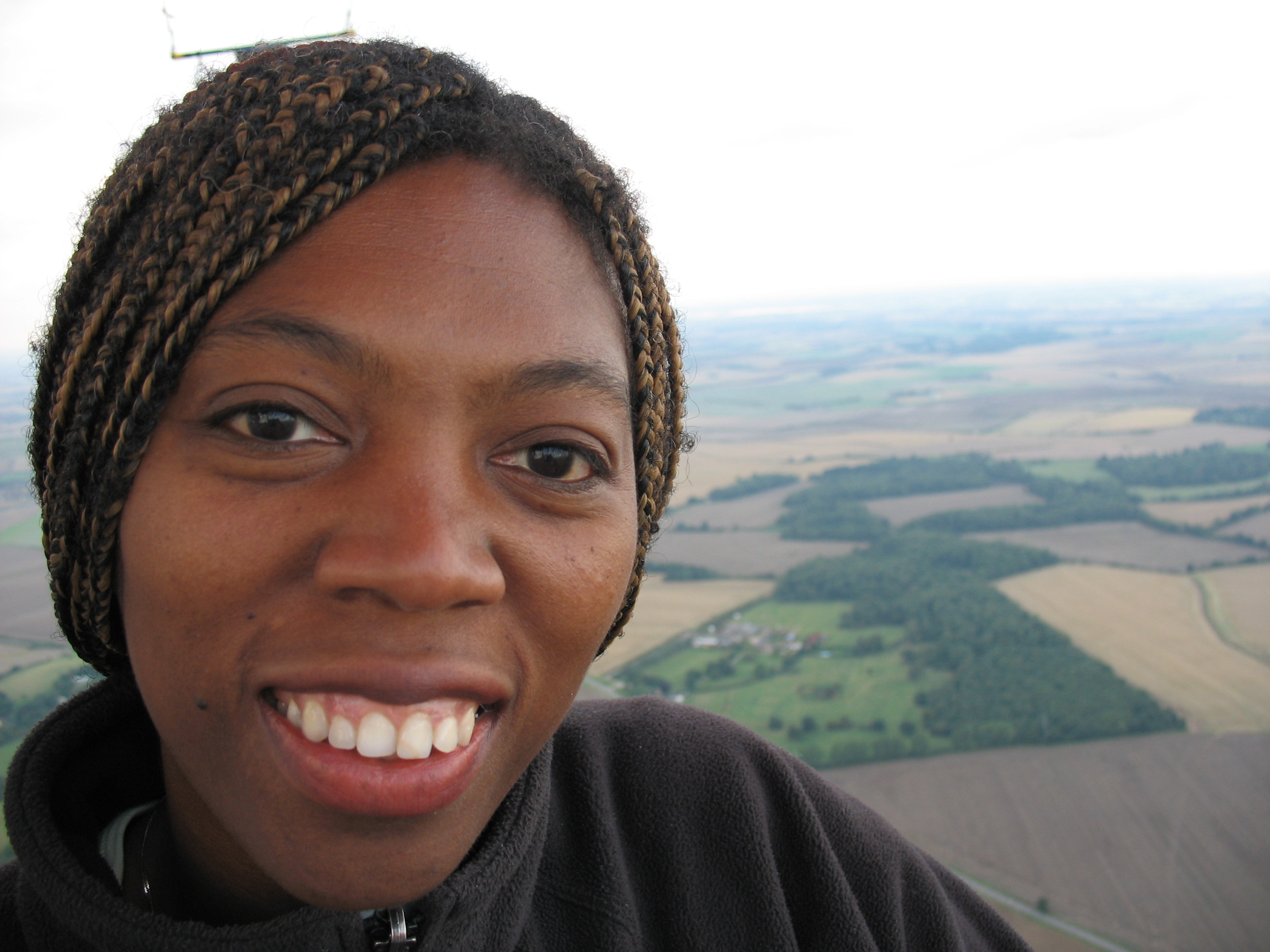An academic smiles at the camera. Behind her is a view of fields from above.