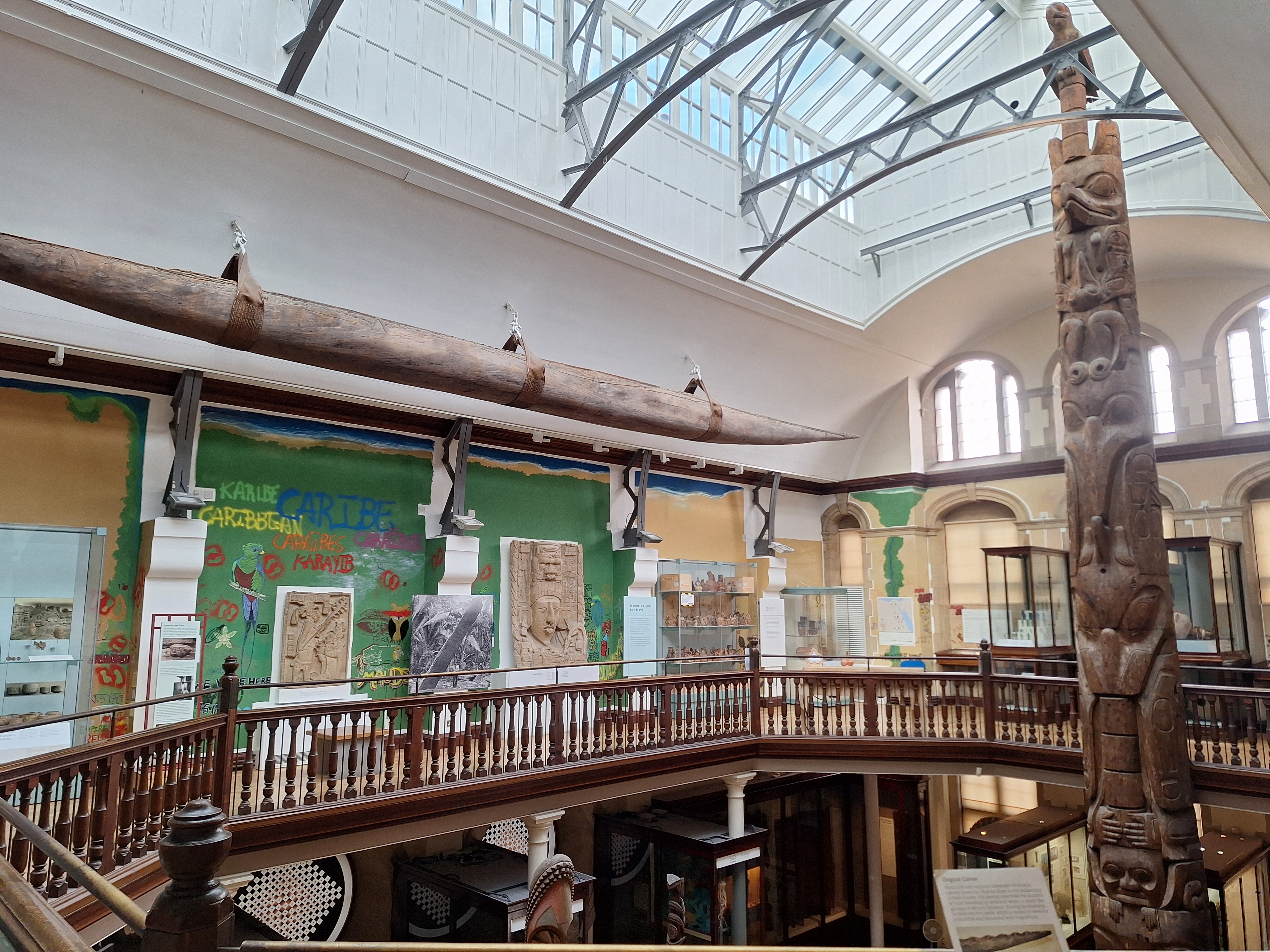 The galleries with sunlight streaming through the glass ceiling. At one end a totem pole rises from the 1st floor through the 2nd floor until it nearly touches the glass overhead. 
