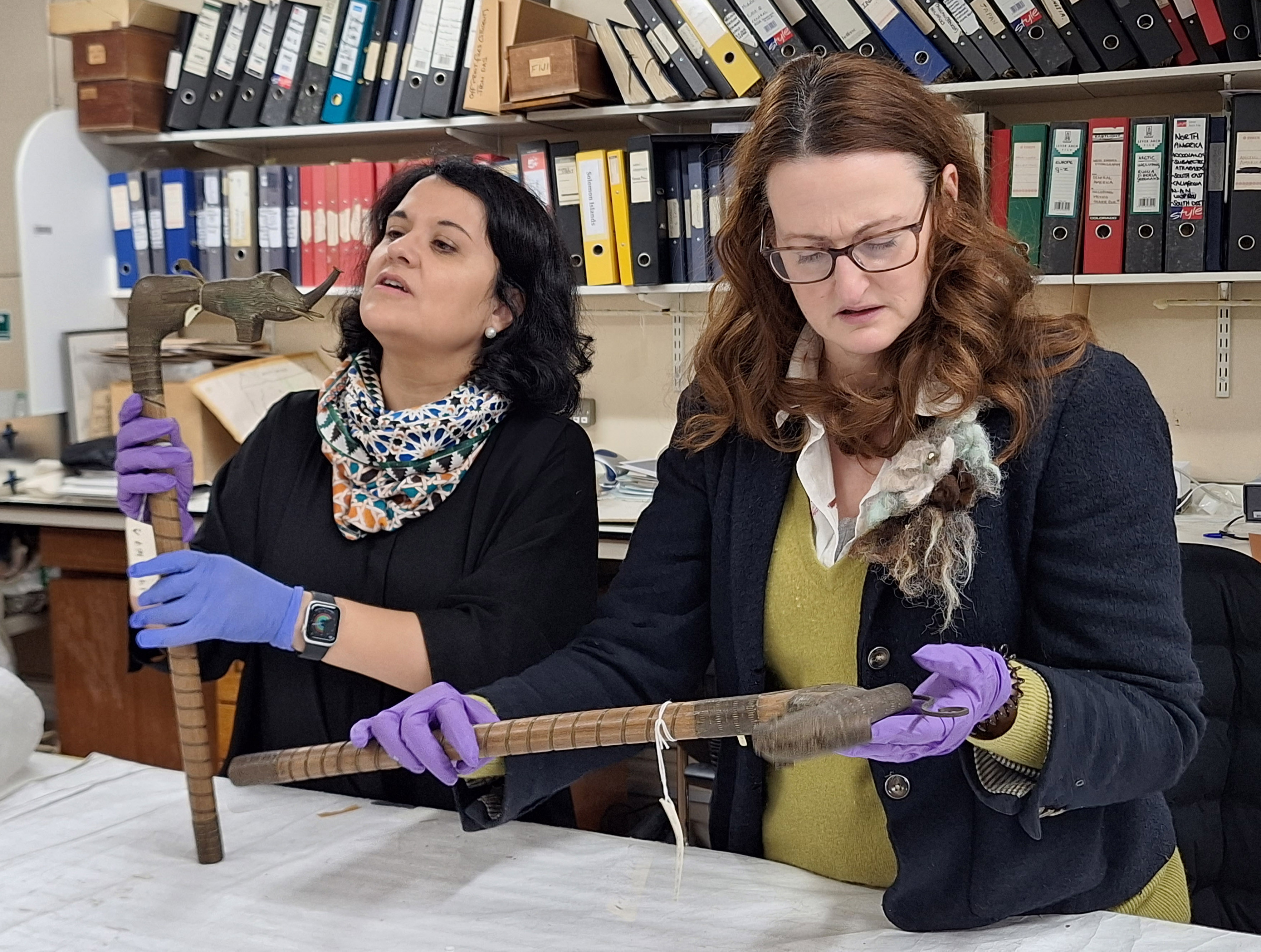A visiting researcher and collections manager holding a pair of short staffs with animal heads, including an elephant.