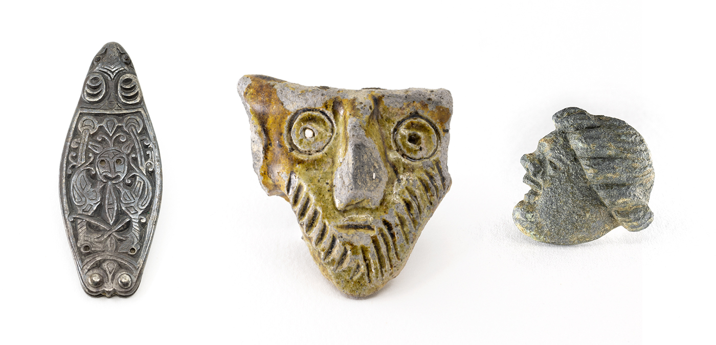 From left to right; silver lozenge shaped strap end featuring a face and two birds facing each other; a bearded face with a yellow/green glaze; male face in profile facing left, with a large chin, upturned nose and a headdress or hairstyle.