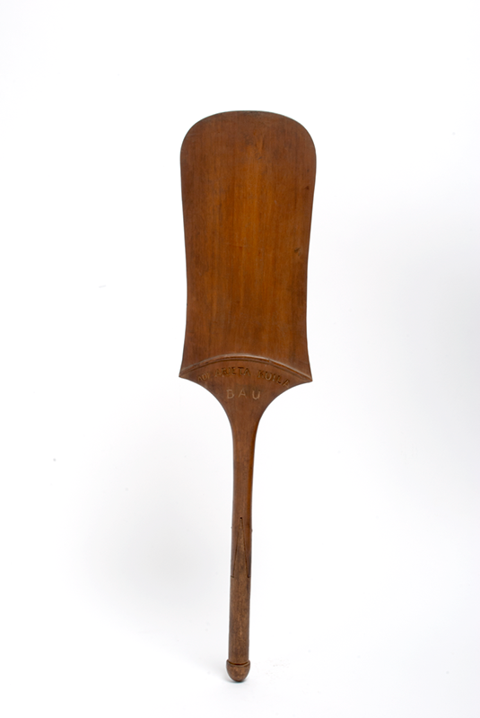 Flat paddle in a rich brown colour, in a rounded rectangular shape. The words 'Adi Arieta Kuila / Bau' have been engraved at the base.
