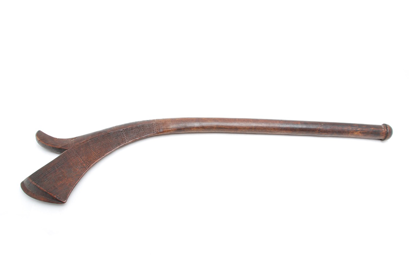 Spurred club of dark wood. The head is broad and carved with lightly raised squares and bands of zigzags.