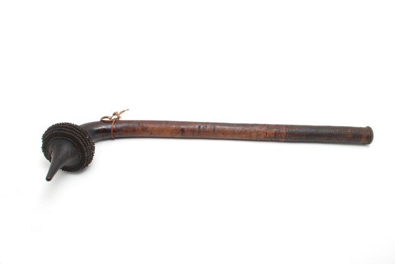 Dark brown club with pointed end, and ridged detailing around this end. Tied with a small cord at the base of the top.