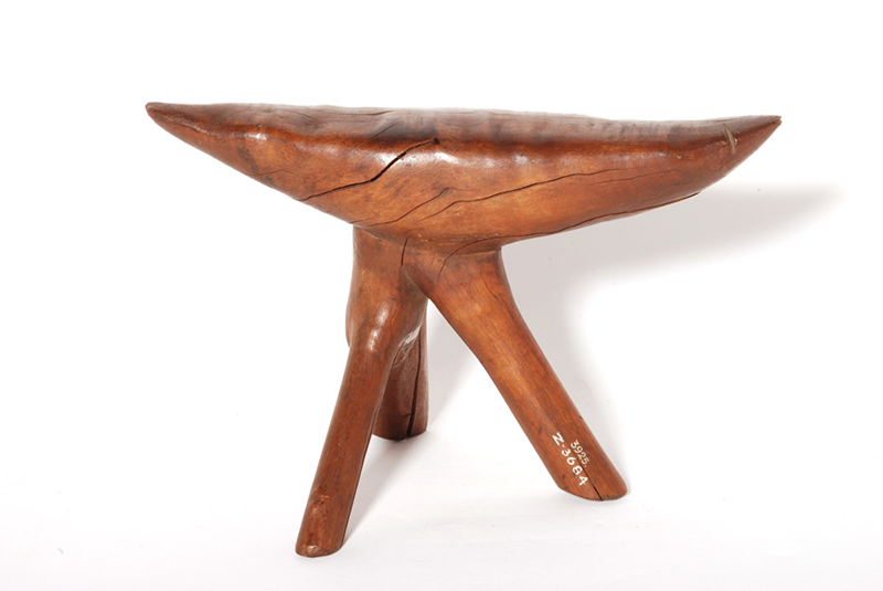 Thick mid brown wooden headrest on a base of with three legs. Made of a single piece, with the wood having minor splits in some areas.
