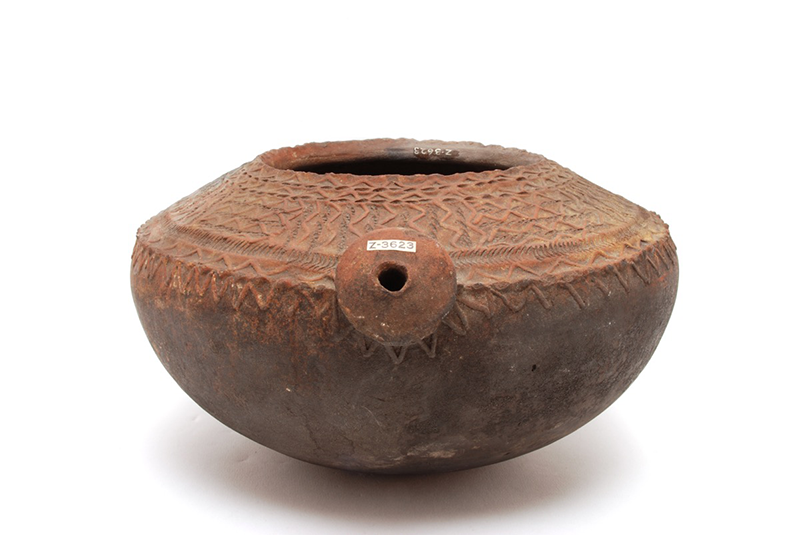 Rounded cooking pot with zig-zag details on the top hand. A spout faces the front.