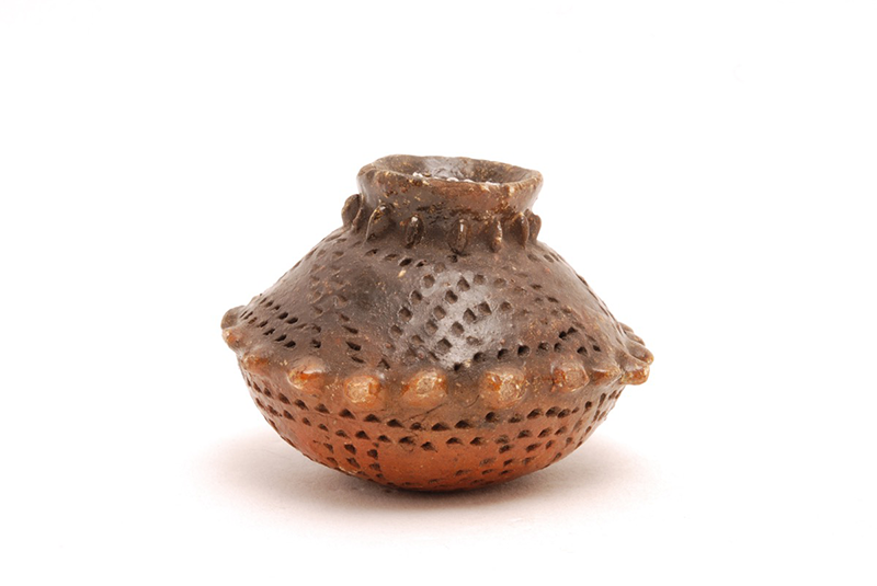 Small glazed ceramic pot, globular in shape, with the neck and the shoulders marked by a line of raised dots. The surface is decoated with incised dots.