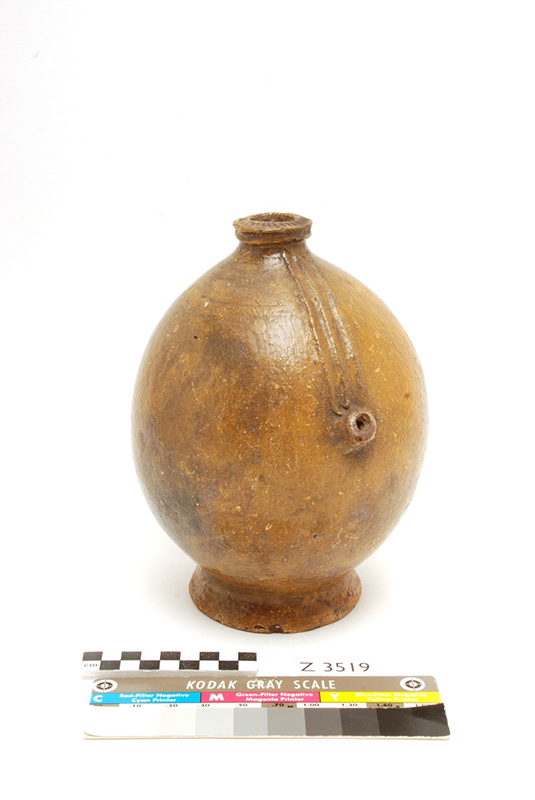 Tall, rounded water pot with a hole in the top and a pouring spout on the side. Undecorated and yellowish in colour.