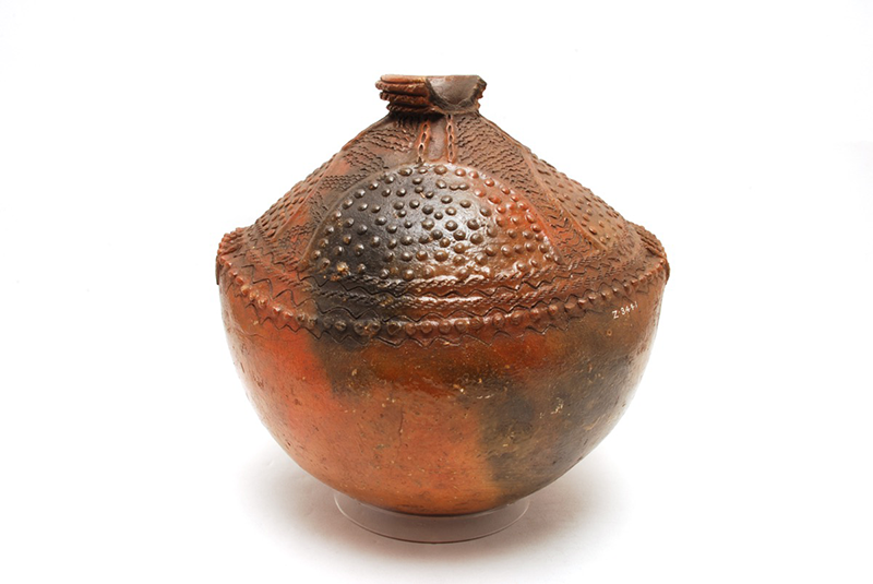 Rounded water jug with concave top half, decorated in raised dots and incisions. Pouring spout at the top.