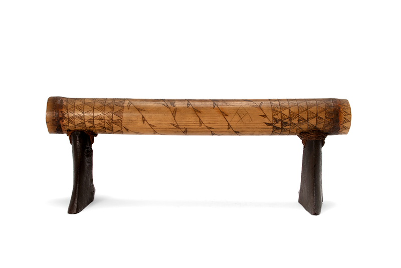 Light wood headrest with darker wood legs. The main piece has leaf design in the centre and geometric triangular patterns on the outer thirds.