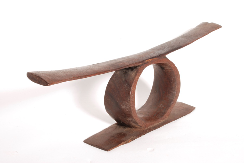 Slightly curved wooden headrest on a central circular stand. The stand is cut out in a circular shape, with a further rectangular base beneath it.