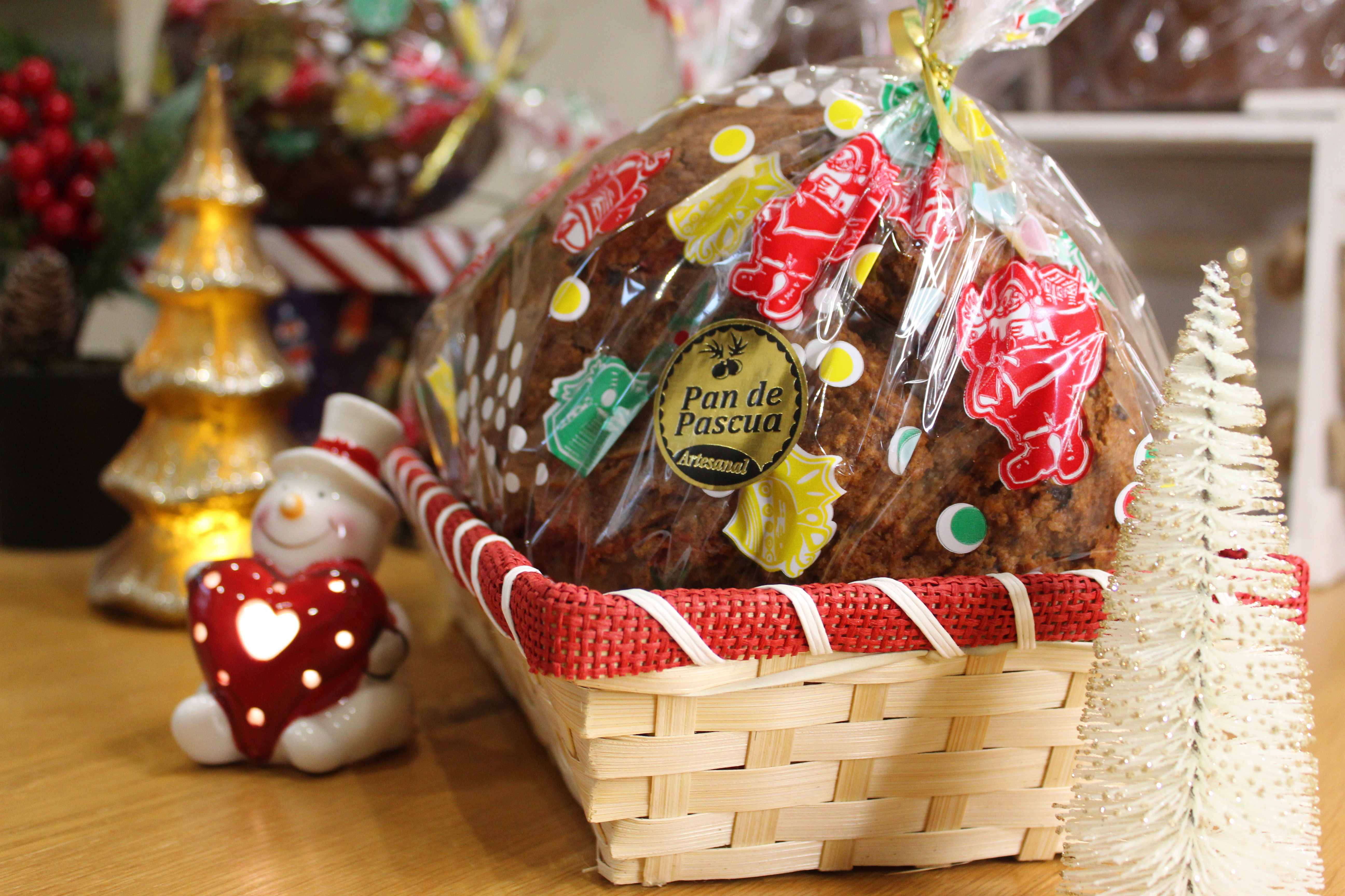 A cellophane wrapped fruitcake sitting in a basket and surrounded by Christmas ornaments.