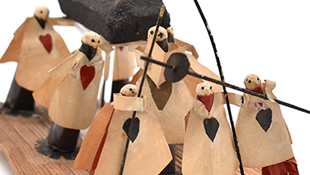 Close up of the funeral procession object, showing the chickpea heads and paper bodies in more detail. Several figures have red, black or gold heart shapes on the front of their costumes.