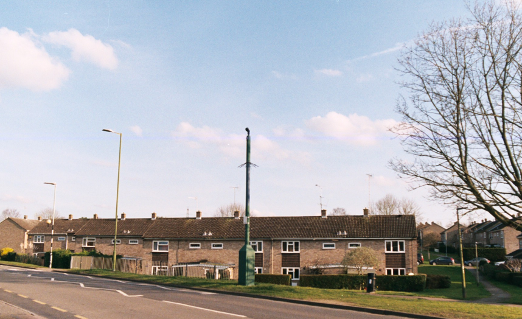 Photograph of a moving surveillance camera within a council estate in Letchworth Garden City. Colour photograph, with a blue, slightly cloudy sky behind.