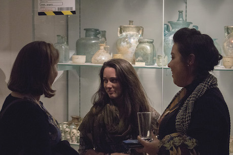 Three visitors converse in front of a glass museum case containing items from the Roman Empire