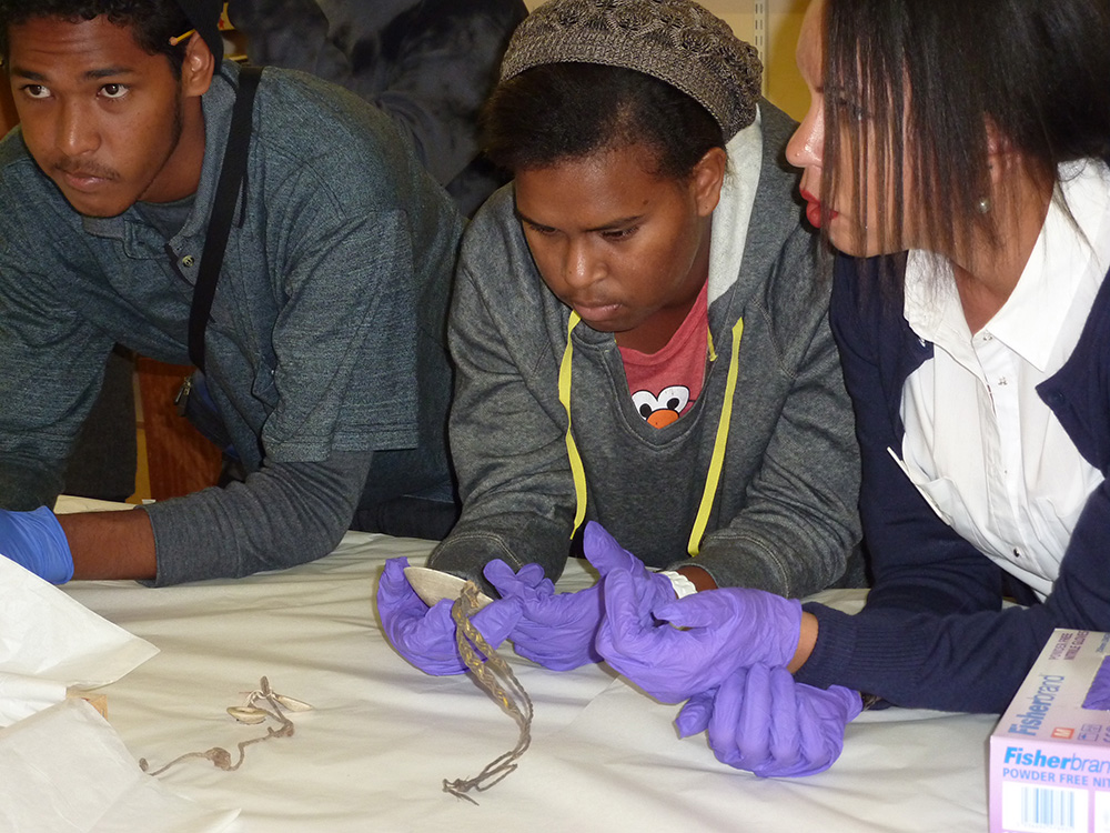 Tagai State College students Stephen Yamashita and Tanisha Pabai with teacher Deborah Belyea looking at a dibidibi shell pendant collected by Alfred Haddon in 1898.