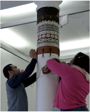 A man and a woman wrap coir cord round a white pillar.