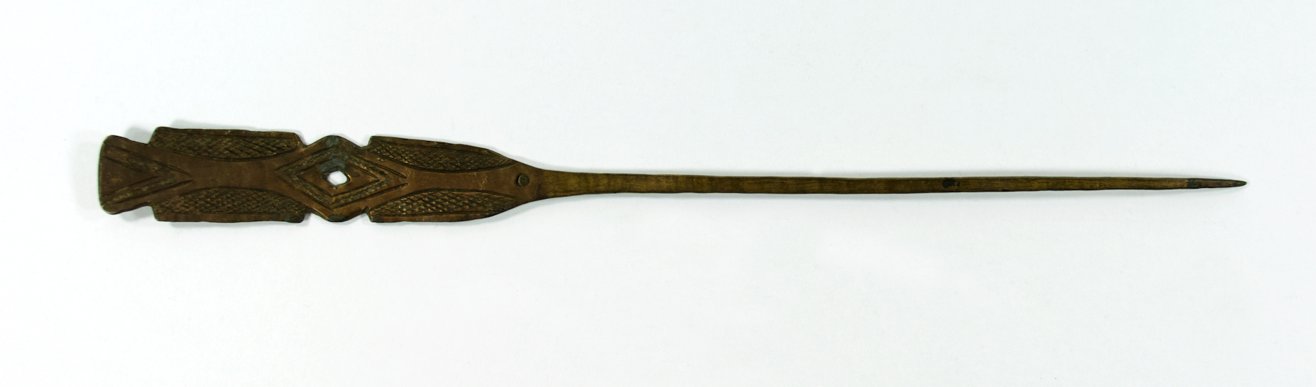  A flat brass hairpin. Decorated with crosshatchings and lines. There is a diamond shape in the middle with dots beaten into it.