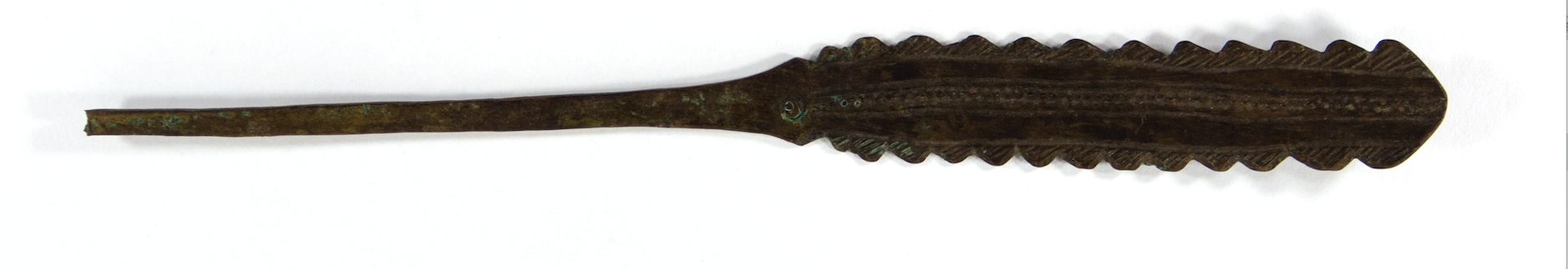  A brass hairpin. The handle is long and flat with serrated edges. It is decorated with patterns formed form lines, circles and dots. 
