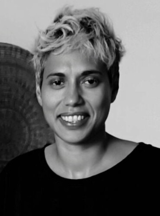 A curator smiles into the camera. The image is black and white and she has short light coloured hair and wears a dark top.