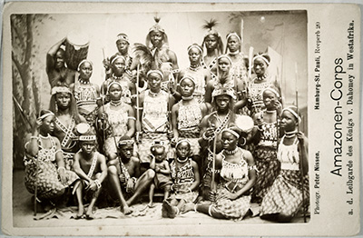a photograph of a group of women from the Dahomey region with a caption that says “Amazonen-Corps a.d. Leibgarde des Konigs v. Dahomey in west Afrika”. 
