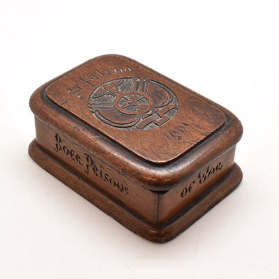 Rectangular wooden box with hinged lid. The top of the lid is inscribed with "St.Helena 1901" and depicts a crest including a bird, lion, and man with rifle; sides of box inscribed with "Made by Boer prisoner of war".