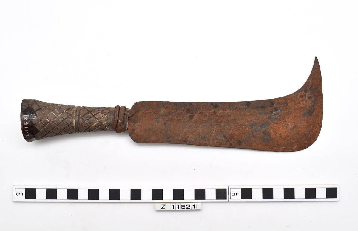 Knife with a flat iron blade, roughly rectangular with a curved protrusion from one corner. Rusted colour.