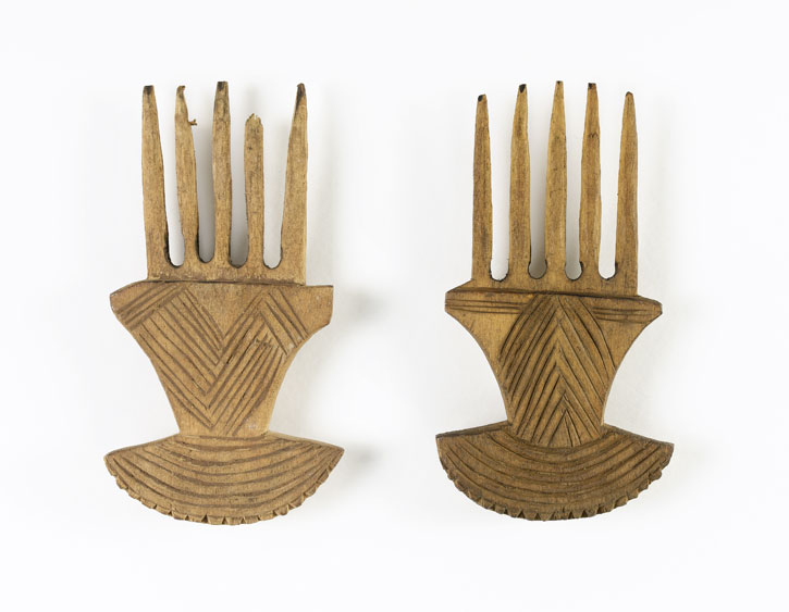  Small wooden comb with five prongs and handle decorated on one side. The handle is fan shaped at the end with a denticulated edges and has incised lines on one side only. 