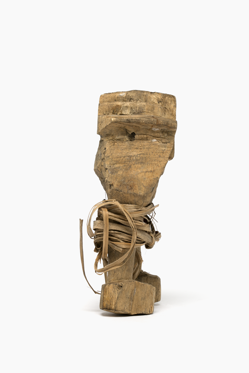 Roughly carved wooden figure representing a man wearing trousers. Plant fibre strips wrapped around the legs. Made of a light wood.