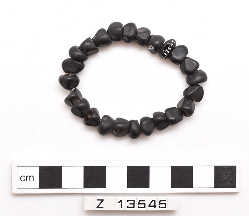 Baby's bracelet. 24 black seeds strung onto cotton. One seed has the number written onto it.