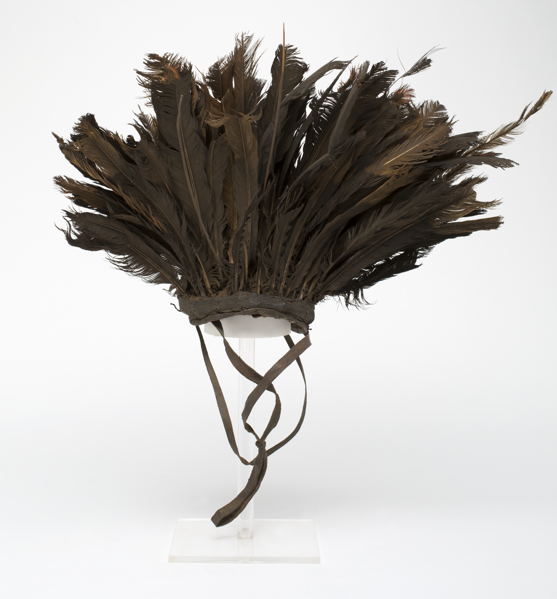 hat with long brown feathers mounted on a leather and cloth cap. Two chin straps attached to the edges.