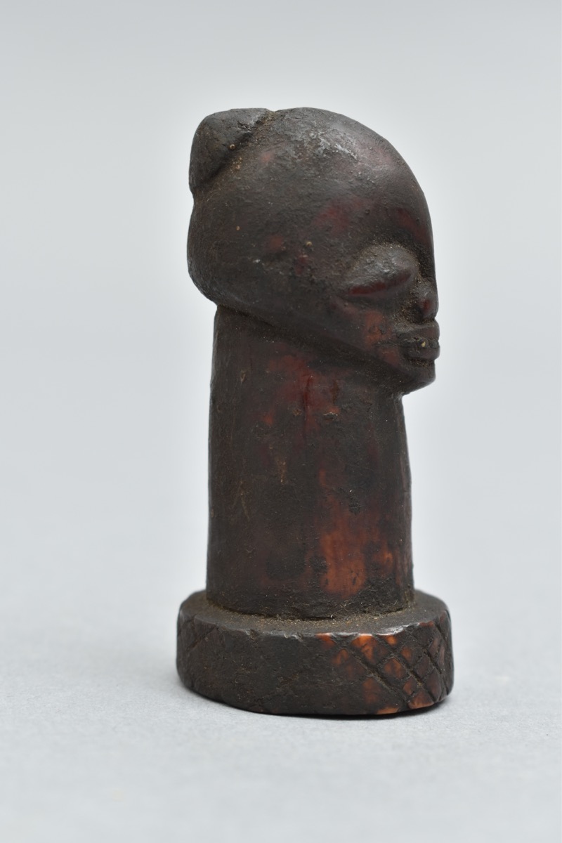 Carving of a human head with long neck on a circular base. The forehead appears elongated with a small cap on the back of the head.