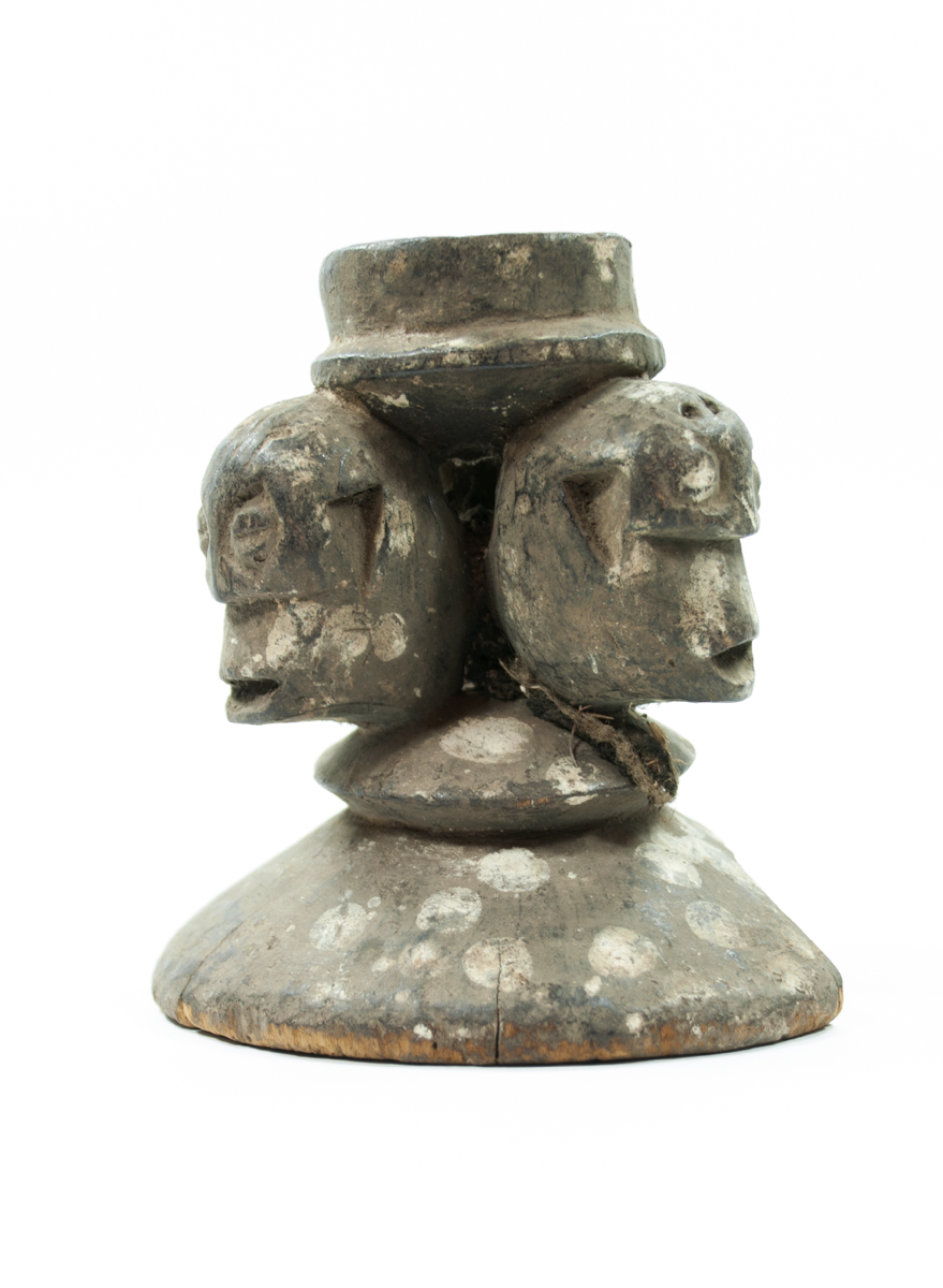 Three carved heads on a larger circular base; covered in black pigment with white spots.