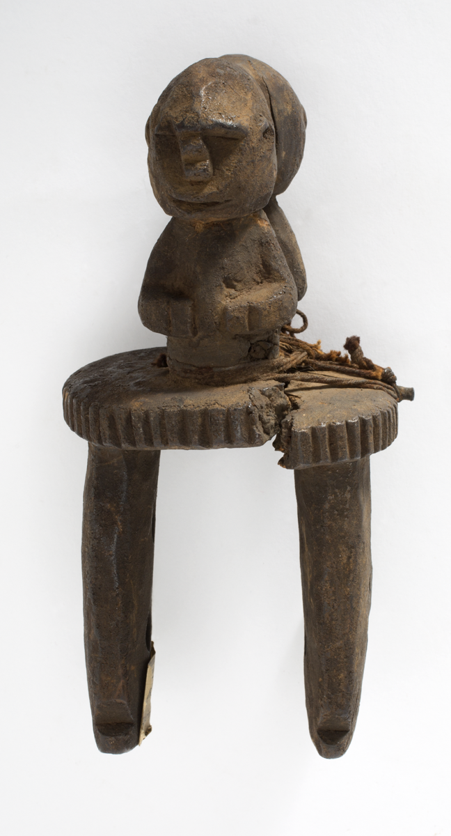 Okeeke. Loom attachment carved from wood. Two human figures from waist up, with hands on belly, arranged back-to-back on top of a serrated disk.