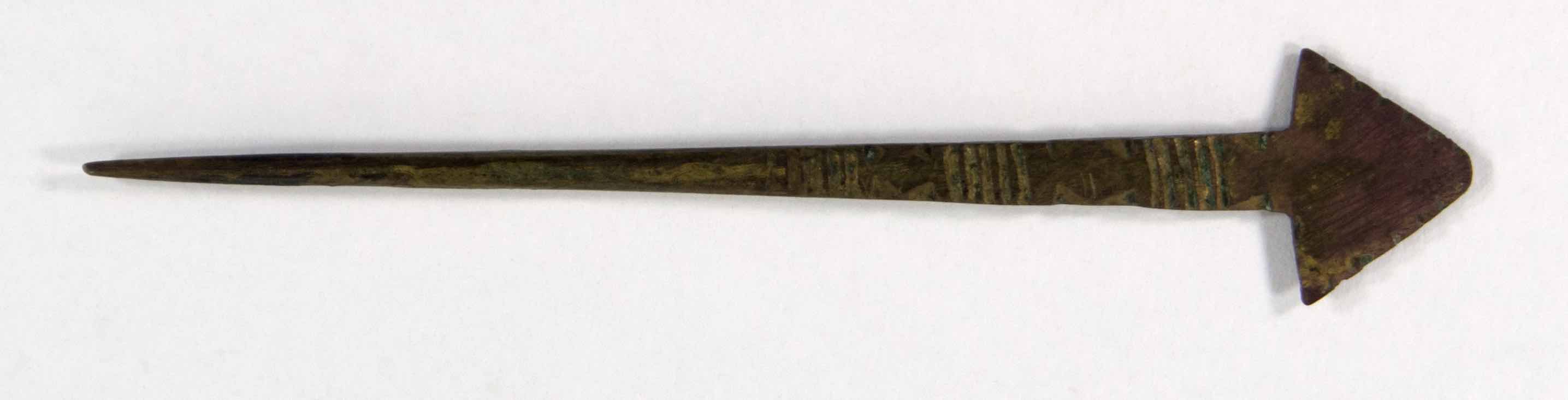 Brass hair pin with round cross section flattening towards a triangular head.