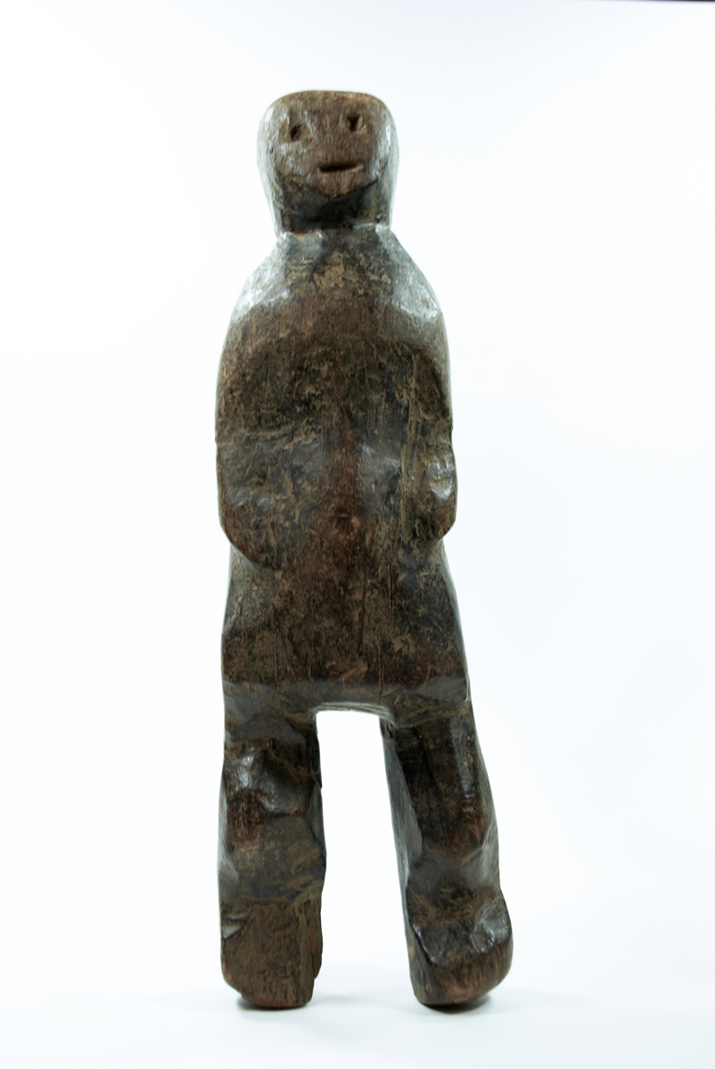 Standing figure with simple facial features; arms faintly carved on body with hands on belly; knees slightly bent. Right foot broken and missing. 