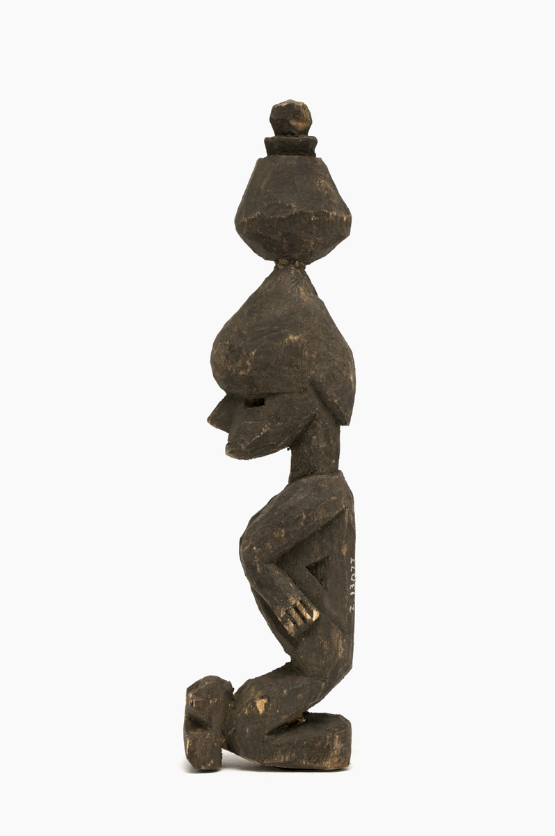 A wooden carving of a kneeling figure with a vessel balanced on top of the head. The figure's arms are by the sides, but with elbows pointing to the front of the body. There is a block depicted in front of the knees.