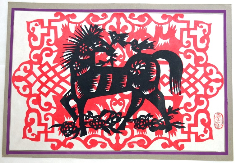 A paper cut artwork featuring a black horse and birds on a red background.