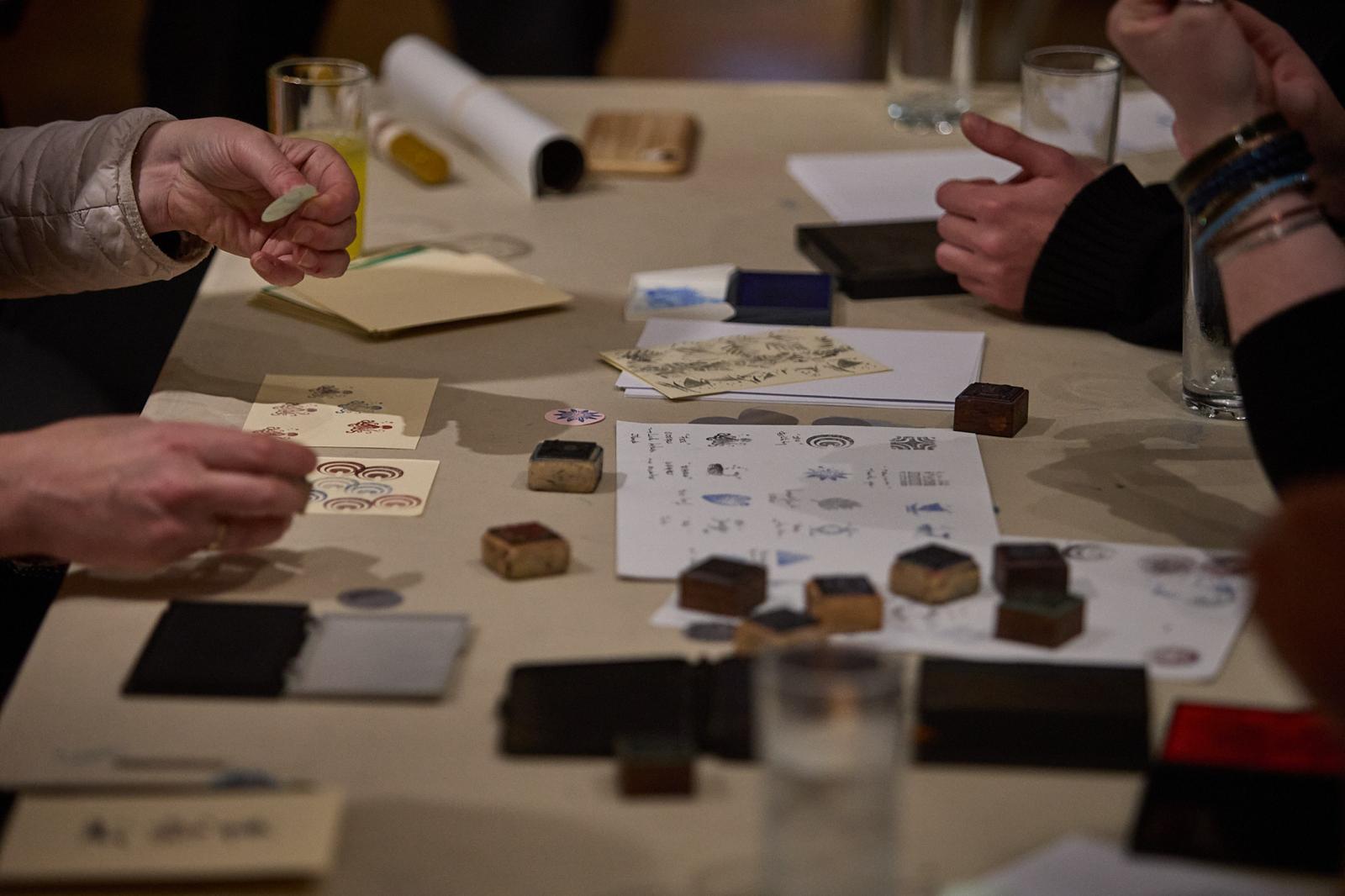 Three pairs of hands take part in a printing activity around a table in the museum galleries.