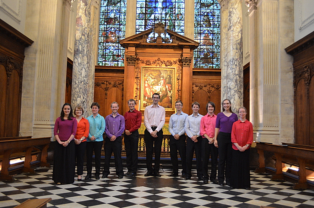 A group of 12 people stand in front of an altar and large stained-glass window.