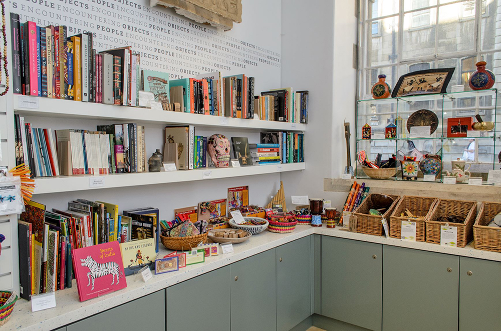 View of the MAA shop, showing books, baskets of objects and objects on stands, above a sage green/grey cabinet with white countertop.