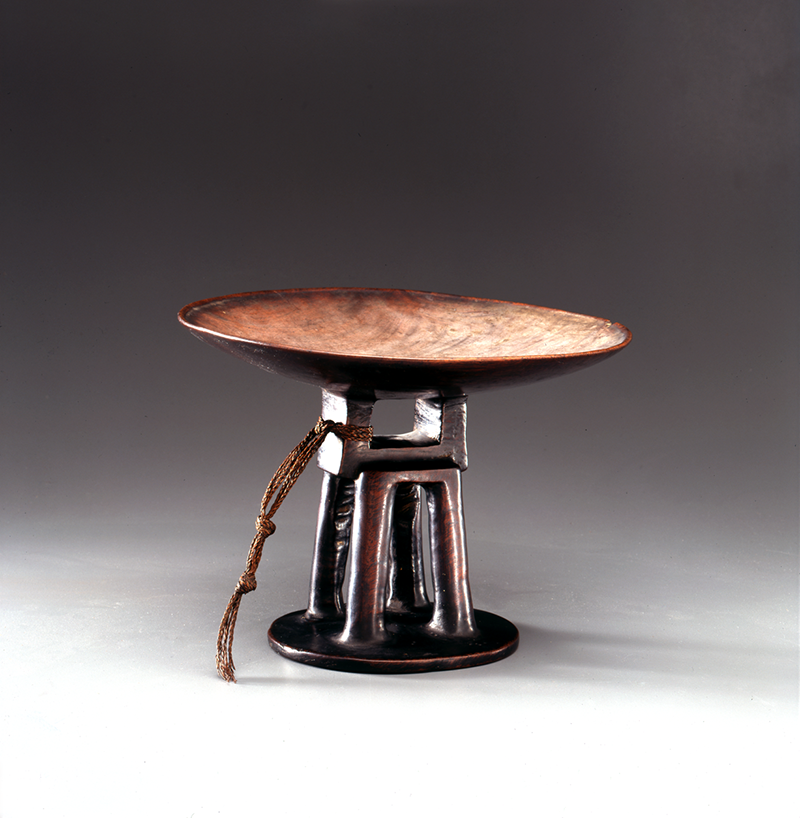 Circular dish carved from a single piece of dark wood, with a pedestal base.