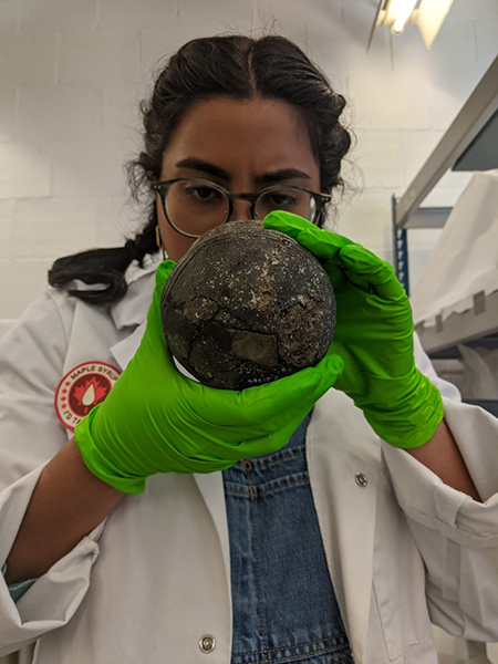 Woman in white coat and gloves holding a medieval urn, analysing it.