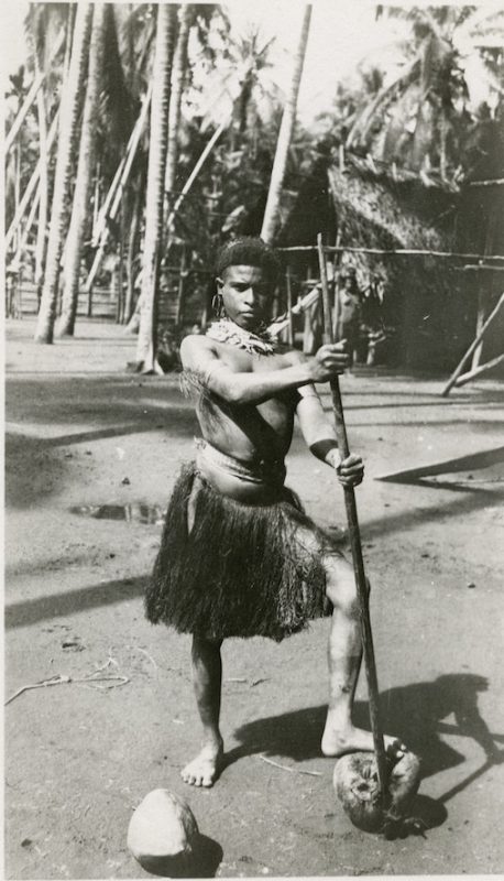 Portrait of a young woman standing with her left foot resting  on a half-opened coconut