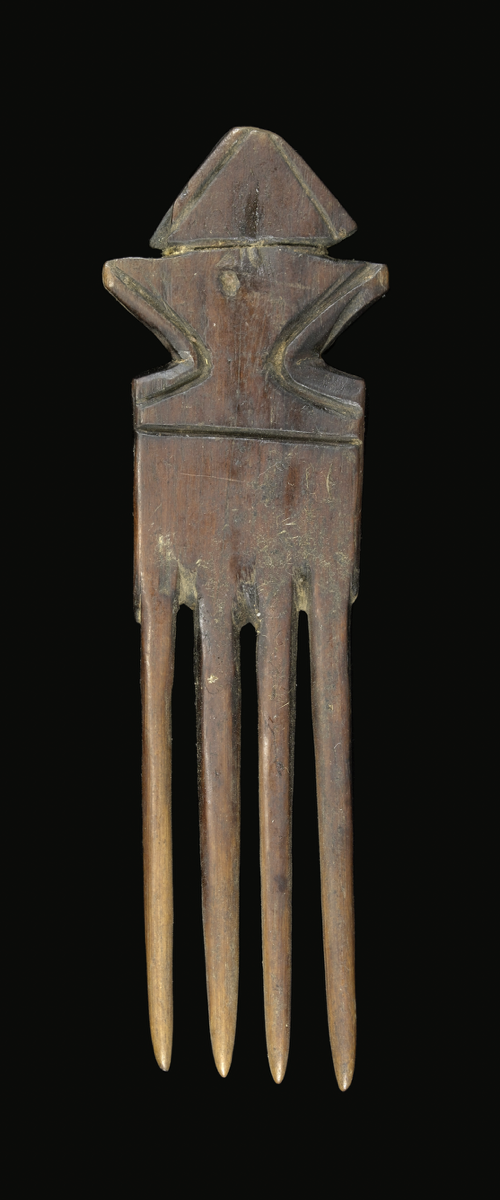 A comb carved from wood with four cylindrical and tapering prongs. The handle has a rectangular section then a constriction from which it flares outward and a triangular shaped terminal. One side is decorated with carved lines.