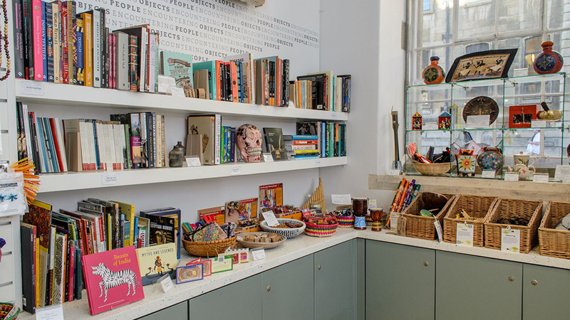 View of the MAA shop, showing books, baskets of objects and objects on stands, above a sage green/grey cabinet with white countertop.