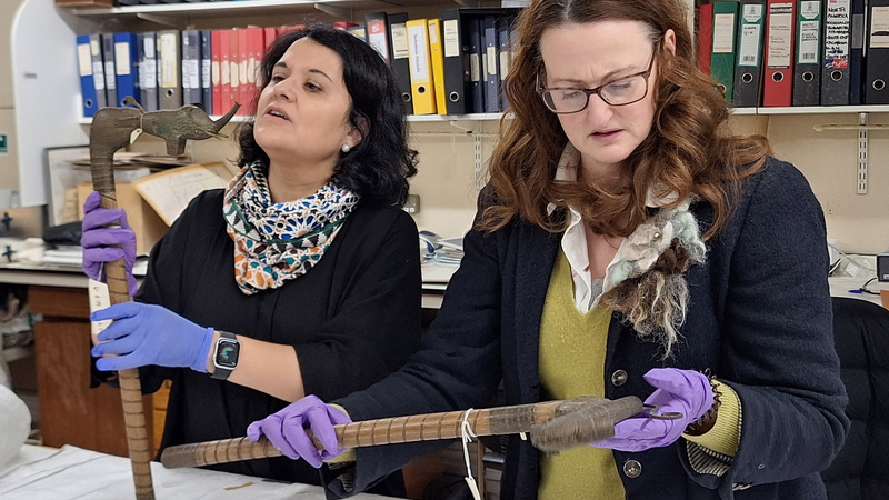 A visiting researcher and collections manager holding a pair of short staffs with animal heads, including an elephant.