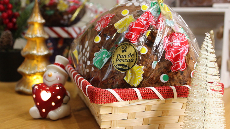 A cellophane wrapped fruitcake sitting in a basket and surrounded by Christmas ornaments.