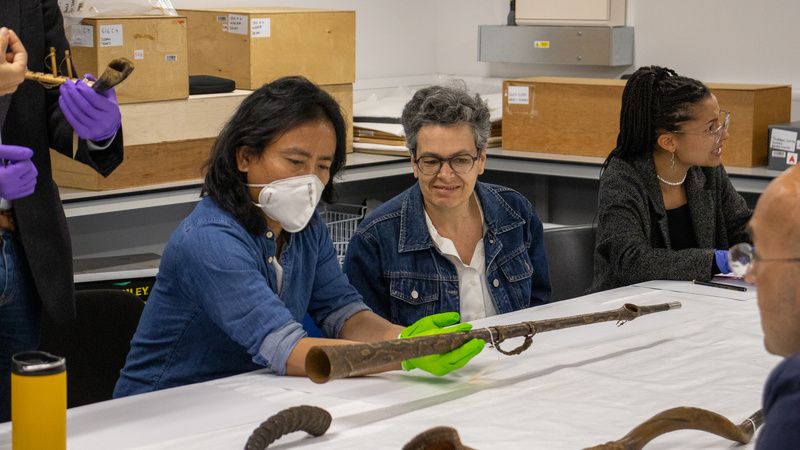 A man and a woman, the man wearing a mask and green latex gloves, look at a musical instrument that the man is handling.