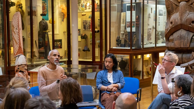 Tony Phillips (left), Temsuyanger Longkumer (centre), and Mark Elliott (right) sit on front of a group of people in the MAA Maudslay Hall. Tony is talking to the group emotively.