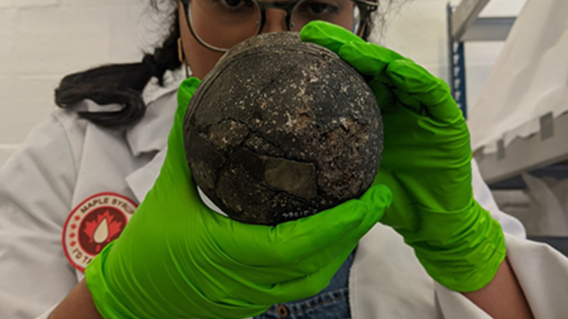 Woman in white coat and green gloves holding a medieval urn, analysing it.